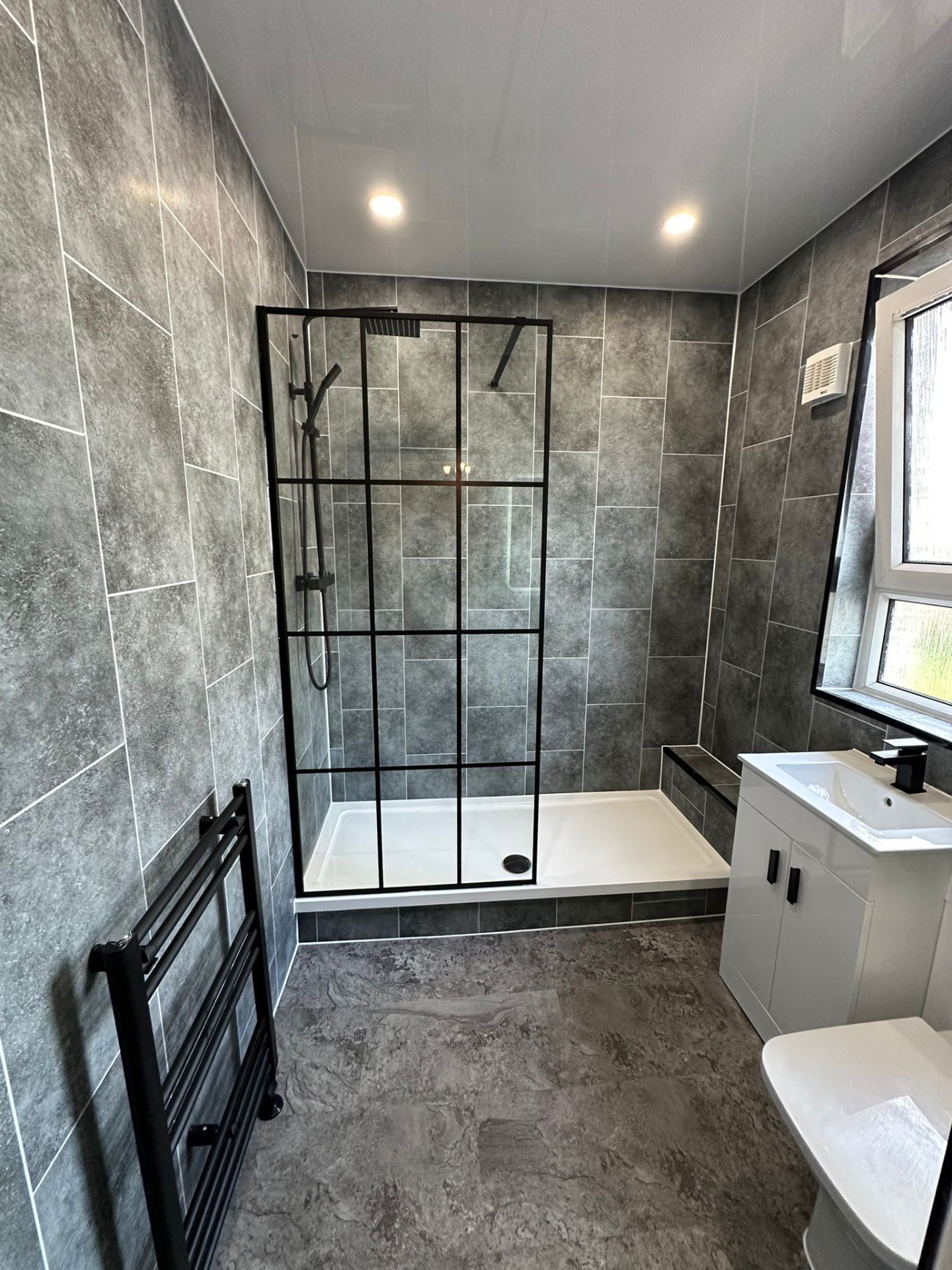 Grey bathroom with a black-framed walk-in shower and white vanity