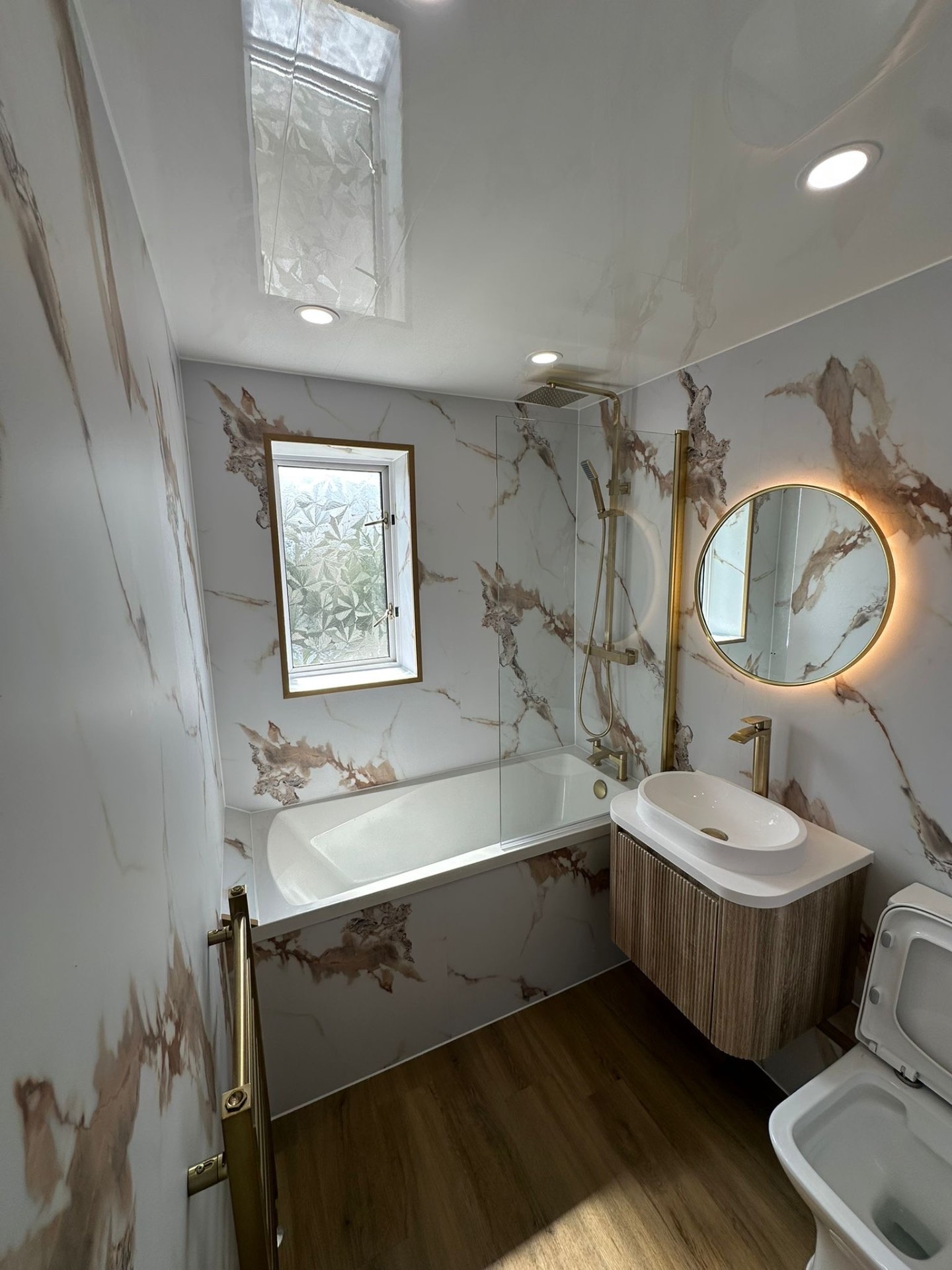A U Builder installation with marble-effect walls, brass fittings and a round illuminated mirror